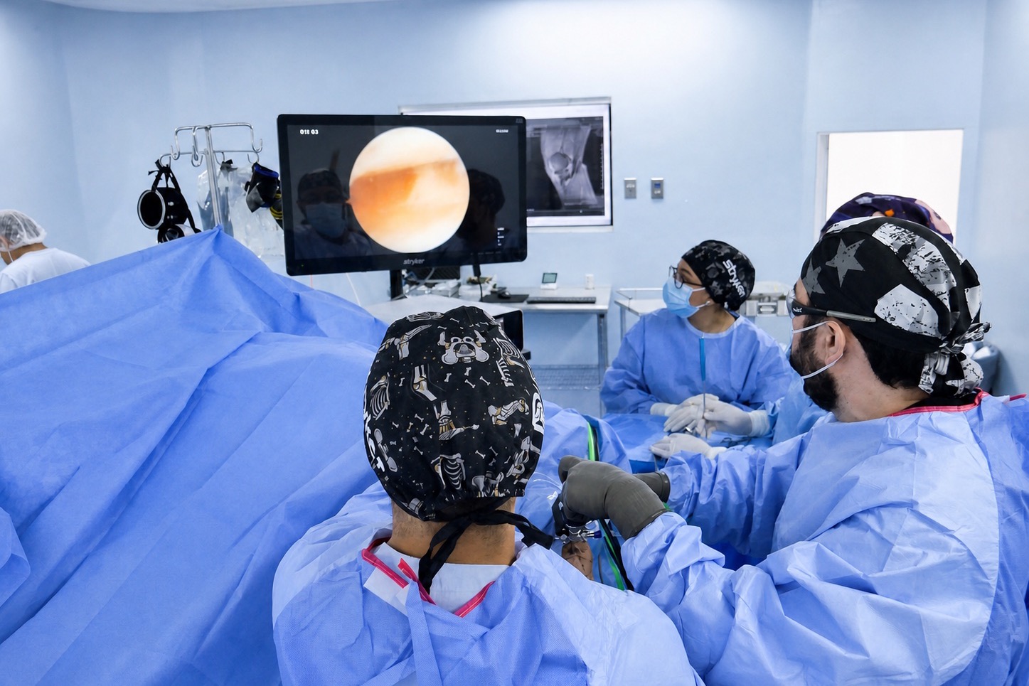 Una artroscopia en marcha: el equipo quirúrgico alrededor de la mesa y la torre mostrando a la vez la imagen del endoscopio y la resonancia del paciente.